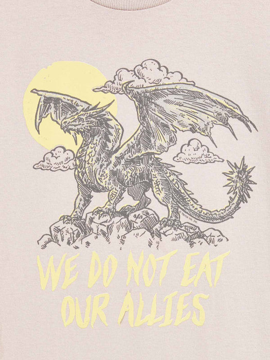 A close-up of a light beige t-shirt featuring a graphic print of a black line-art dragon under a yellow sun and clouds, with the text 'WE DO NOT EAT OUR ALLIES' printed below in yellow.