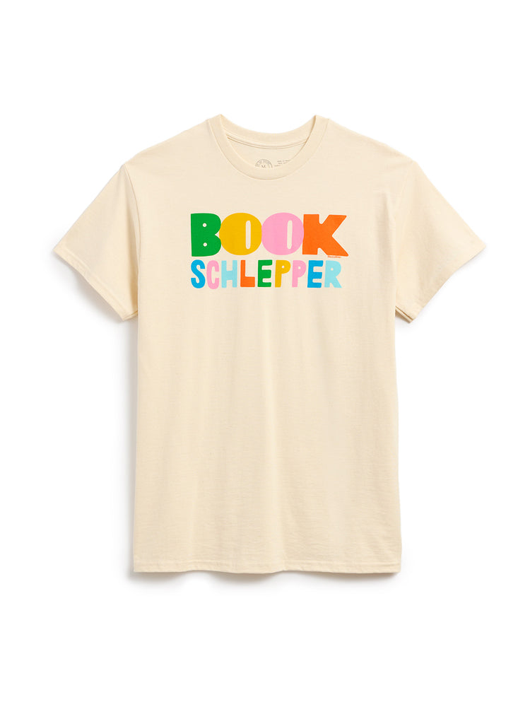 A light beige crewneck t-shirt featuring a colorful graphic print on the chest that reads 'BOOK SCHLEPPER' in playful, multicolored letters, displayed against a clean white background.