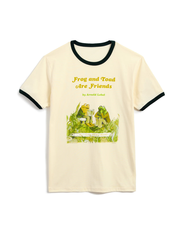 A cream-colored ringer t-shirt with forest green trim on the collar and sleeve cuffs, featuring a colorful graphic of a frog and toad sitting on grass with the text 'Frog and Toad Are Friends' by Arnold Lobel.