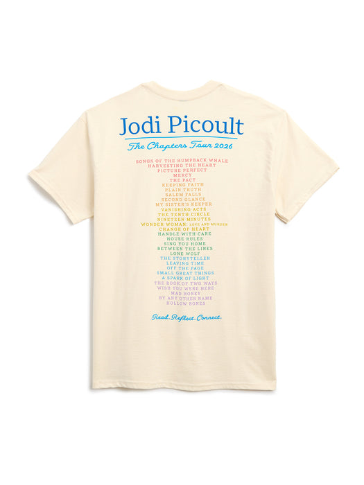 The back of a cream-colored t-shirt featuring a large blue 'Jodi Picoult The Chapters Tour 2026' and a multi-colored list of her books printed in the center, set against a plain white background.