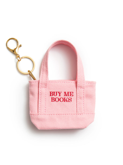 A small pink canvas tote keychain bag with gold-tone keyring hardware and red embroidered text reading 'BUY ME BOOKS' on the front, shown on a clean white background.