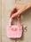 A hand holds a small pink canvas book bag keychain with the words 'BUY ME BOOKS' in red, attached to a gold key ring, against a light wood plank background.