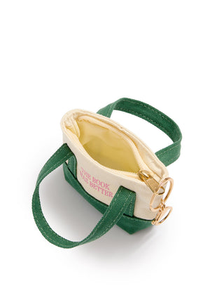 A small canvas shoulder bag with a cream exterior, green handles, a green base, and gold-tone hardware, shown on a white background. The side of the bag has pink text that reads 'THE BOOK WAS BETTER'.