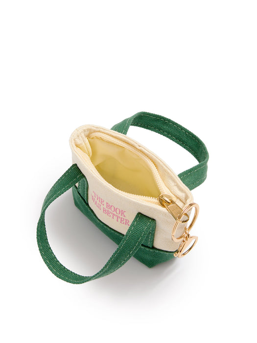 A small canvas shoulder bag with a cream exterior, green handles, a green base, and gold-tone hardware, shown on a white background. The side of the bag has pink text that reads 'THE BOOK WAS BETTER'.