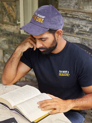 Man wearing a cap and t-shirt with text, reading a book outdoors.