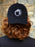 Person wearing a black cap with a white logo on a blurred background