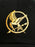 Close-up of a black baseball cap featuring a gold embroidered Hunger Games Mockingjay logo.