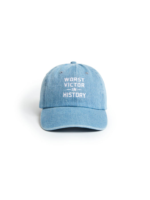 A light blue denim baseball cap with white embroidered text reading 'WORST VICTOR IN HISTORY' on the front, shown against a plain white background.