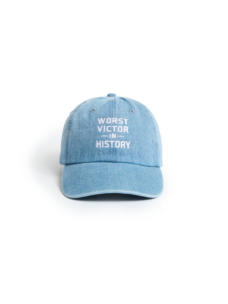 A light blue denim baseball cap with white embroidered text reading 'WORST VICTOR IN HISTORY' on the front, shown against a plain white background.