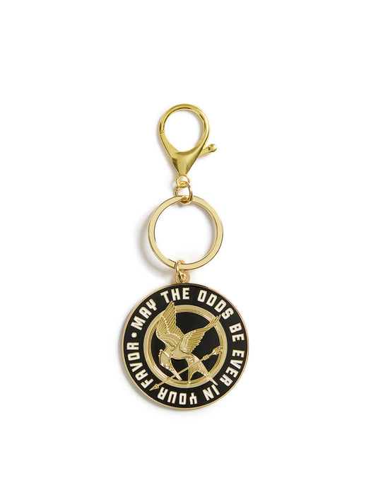 Gold keychain with black circular emblem featuring text and a logo on a white background