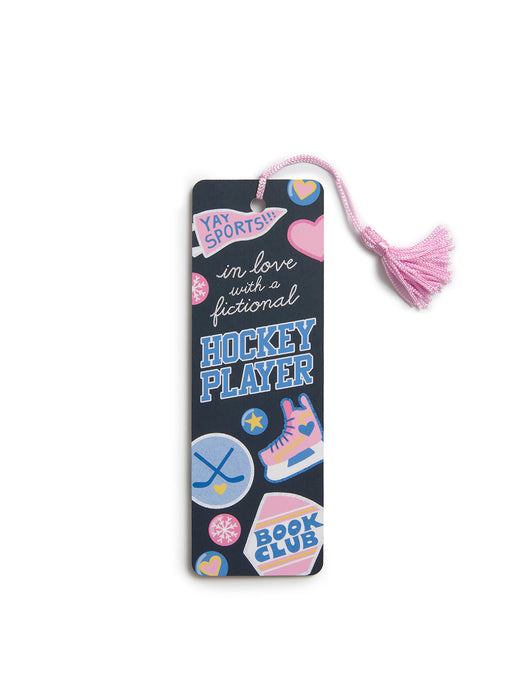 A dark navy book bookmark with a pink tassel, decorated with various colorful hockey-themed stickers and text that reads 'in love with a fictional HOCKEY PLAYER'.