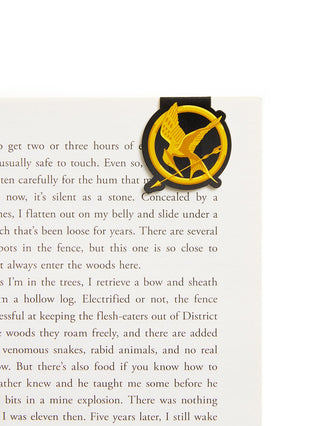 A black and gold mockingjay magnetic bookmark resting on a page of a book.