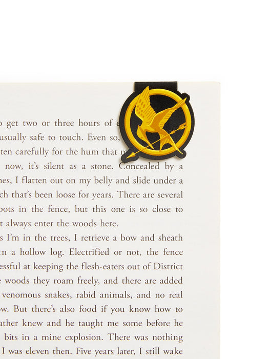 A black and gold mockingjay magnetic bookmark resting on a page of a book.