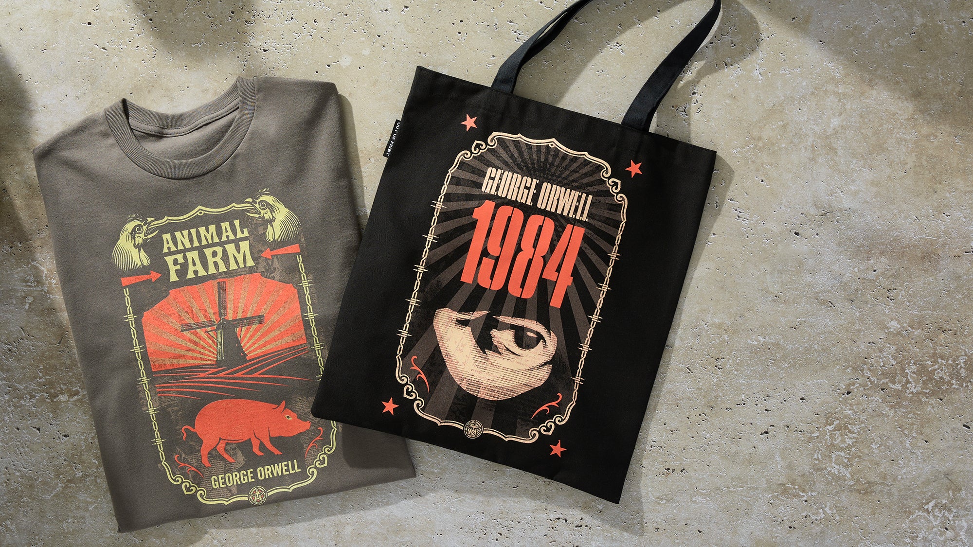 A folded dark gray T-shirt and a black tote bag with matching handles, both printed with a vintage-style George Orwell graphic reading 'Animal Farm and 1984' and laid on a textured concrete surface.