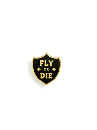 A small shield-shaped enamel pin with a black face, gold border, and gold lettering that reads 'FLY OR DIE' on a plain white background.