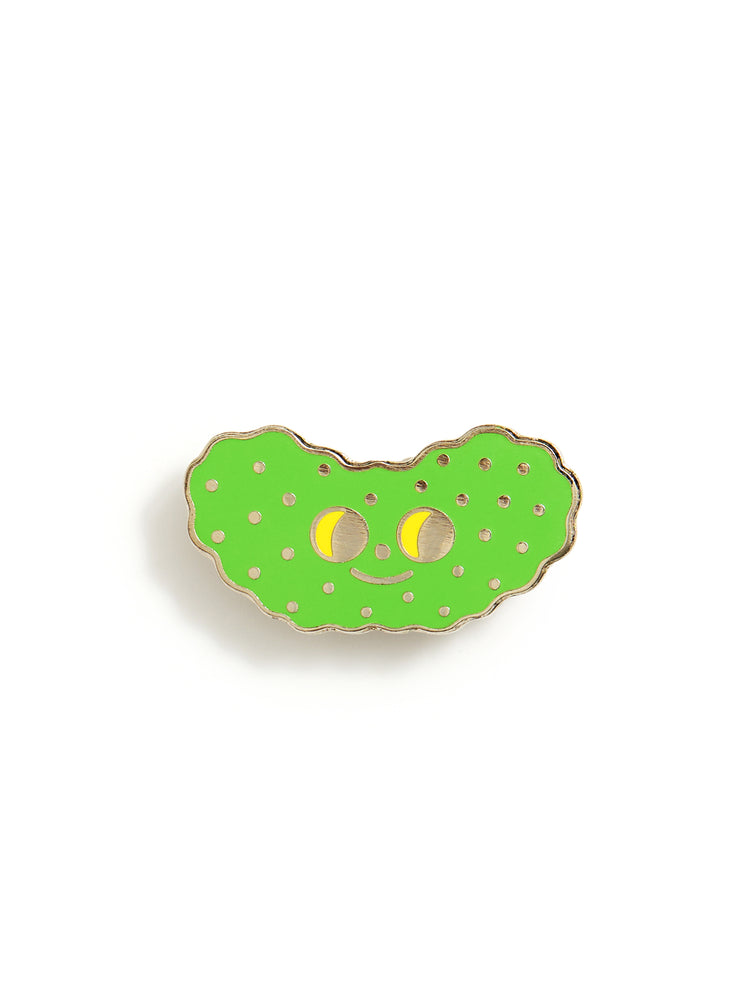 A green pickle-shaped enamel pin with yellow eyes and a gold-tone outline, shown on a plain white background.