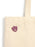 A close-up of a cream canvas tote bag with a small purple and gold Basgiath Iron Club shield-shaped pin on the front, set against a plain white background.