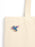 A close-up of a cream canvas tote bag with a small colorful dragon enamel pin on the front, set against a plain white background.