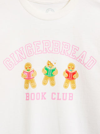 A close-up of a white crewneck t-shirt featuring a colorful graphic print. The design displays the words 'GINGERBREAD BOOK CLUB' in pink lettering, with three gingerbread characters reading books in the center.