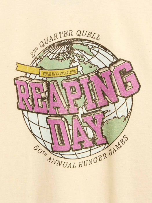 A close-up of a beige garment featuring a large graphic print for the 50th Annual Hunger Games, titled 'Reaping Day,' with a globe illustration and pink lettering.