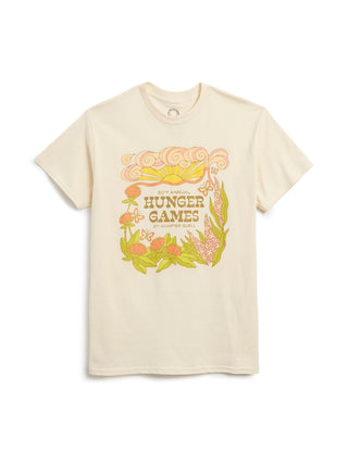 A cream-colored short-sleeve t-shirt featuring a colorful graphic print on the front with the text 'HUNGER GAMES' and stylized illustrations of a sun, butterfiles, and flowers.