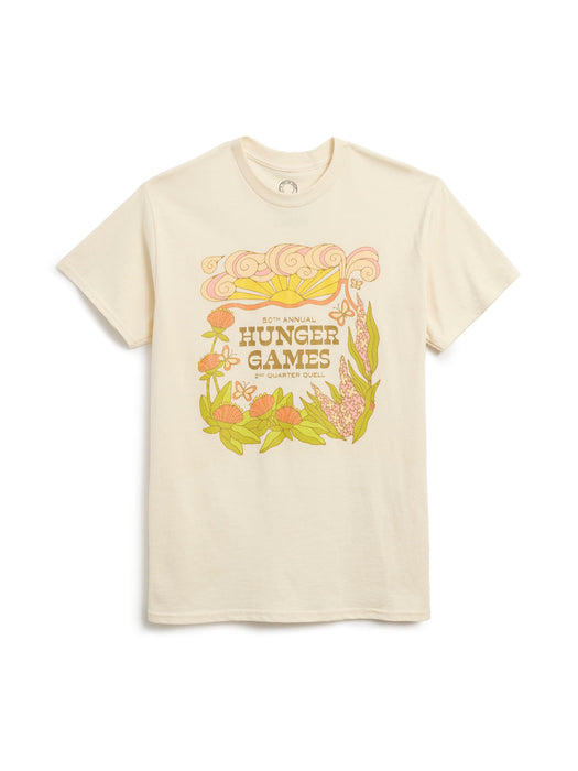 A cream-colored short-sleeve t-shirt featuring a colorful graphic print on the front with the text 'HUNGER GAMES' and stylized illustrations of a sun, butterfiles, and flowers.