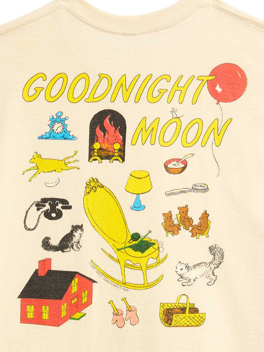 A close-up of a cream-colored t-shirt featuring a colorful graphic print with the text 'GOODNIGHT MOON' and various whimsical illustrations including a rocking chair, house, telephone, and balloons.