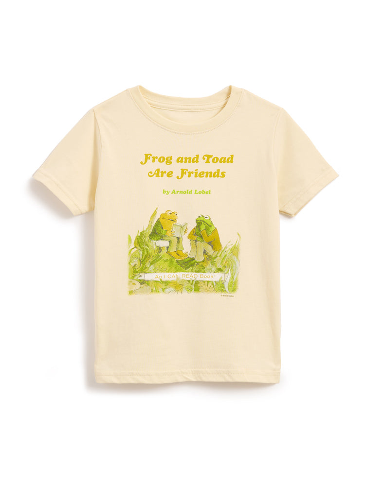 A cream-colored short-sleeve t-shirt featuring a graphic print of a green frog and a yellow-green toad sitting on a log, with the text 'Frog and Toad Are Friends' and 'by Arnold Llobel' printed above them.