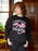 Person wearing a black sweatshirt with a dragon graphic and text in a room with wooden paneling.
