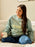 Woman wearing a light blue sweatshirt with 'BOOKS' printed on it, sitting on a couch holding a mug.