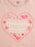 A close-up of a light pink t-shirt featuring a heart-shaped graphic with the words 'crying over a FICTIONAL COWBOY' in white and pink, surrounded by cowboy hat, horseshoe, star, and flower illustrations.
