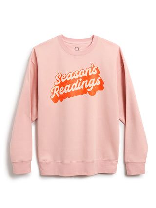 A light pink crewneck sweatshirt featuring a retro-style graphic on the chest that reads 'Season's Readings' in bubble lettering, displayed against a clean white background.