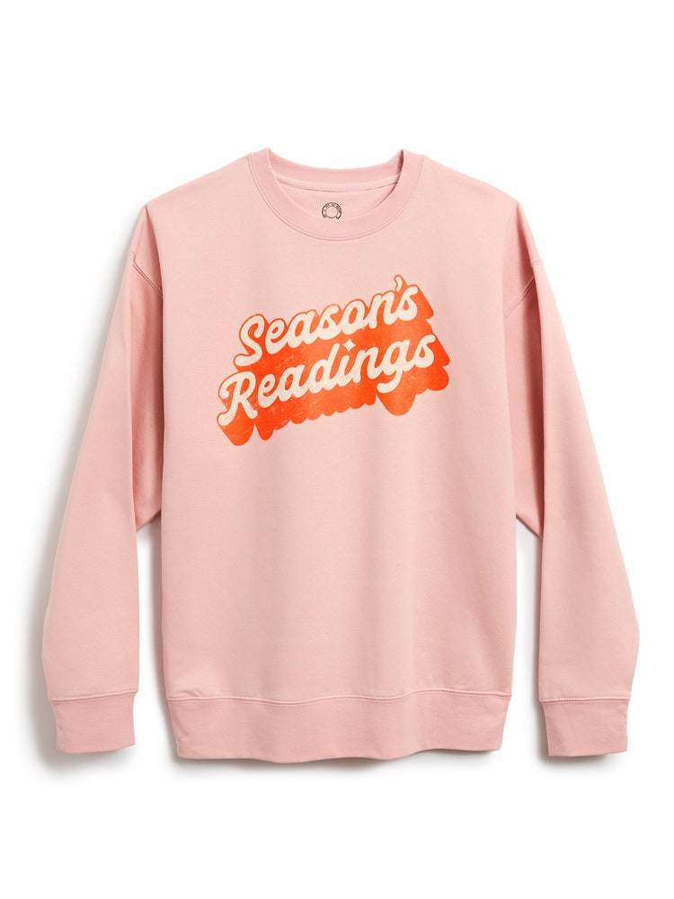 A light pink crewneck sweatshirt featuring a retro-style graphic on the chest that reads 'Season's Readings' in bubble lettering, displayed against a clean white background.