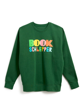 A dark green crewneck sweatshirt featuring the text 'BOOK SCHLEPPER' printed across the chest in a colorful, playful font with letters in green, yellow, orange, and blue.