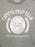 Close-up of a heather gray crewneck t-shirt featuring a distressed white graphic print that reads 'CAPITOL PREP TEAM' with a central Hunger Games emblem and the phrase 'Here to make you gorgeous'.