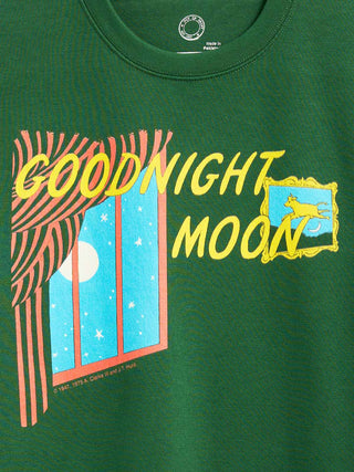 A close-up of a green t-shirt featuring a retro graphic print with the text 'GOODNIGHT MOON' in yellow, a window showing a blue night sky with stars and a moon, and a yellow cow in a frame.