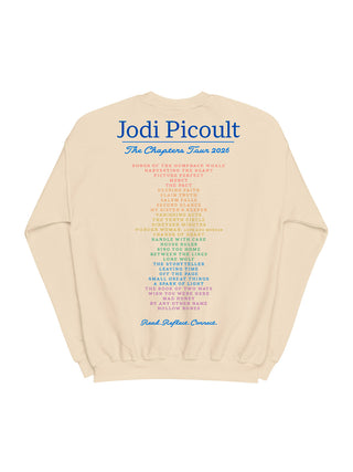A cream-colored crewneck sweatshirt featuring a large blue and multicolor printed text graphic on the back, reading 'Jodi Picoult The Chapters Tour 2026'.