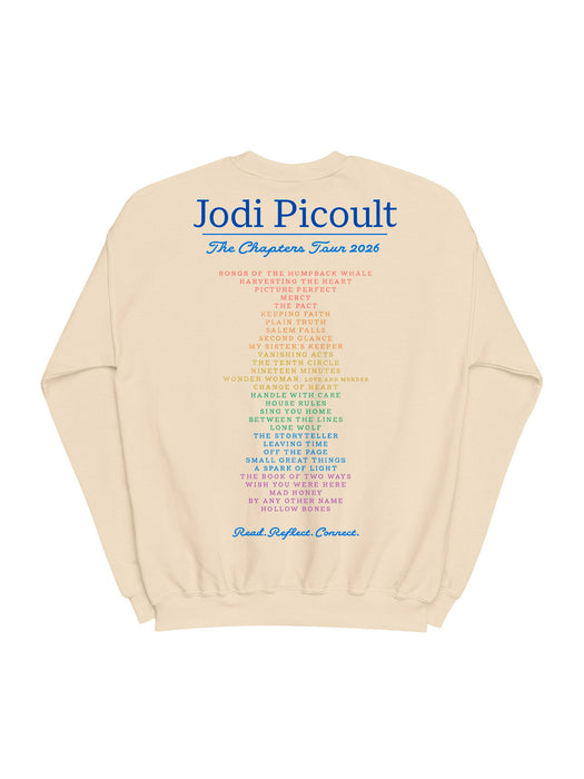 A cream-colored crewneck sweatshirt featuring a large blue and multicolor printed text graphic on the back, reading 'Jodi Picoult The Chapters Tour 2026'.