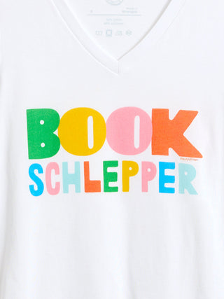 White V-neck t-shirt featuring a colorful graphic print that reads 'BOOK SCHLEPPER' in bold, multicolored letters.