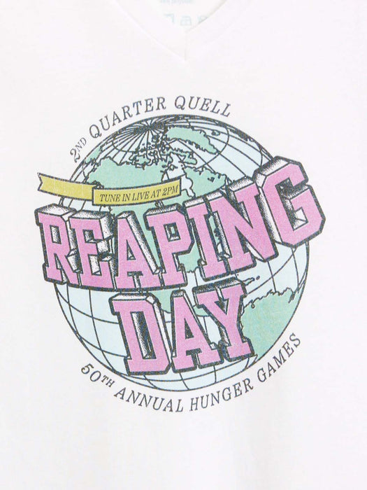 A close-up of a white garment featuring a graphic print for the 50th Annual Hunger Games 'Reaping Day' event. The design includes a globe illustration with pink 3D text reading 'REAPING DAY' and smaller black text reading '2ND QUARTER QUELL' and '50TH ANNUAL HUNGER GAMES'.