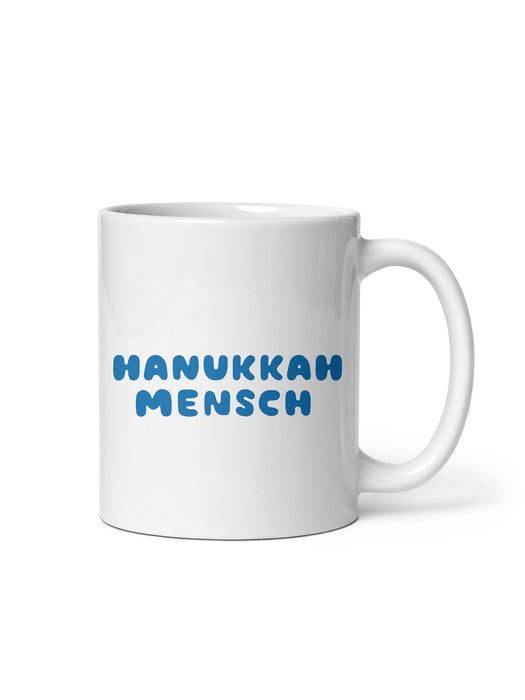 A white ceramic mug with the phrase 'HANUKKAH MENSCH' printed in blue rounded letters on the front, set against a plain white background.
