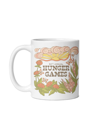A white ceramic mug featuring a retro-style graphic design for the 50th Annual Hunger Games, with stylized flowers, leaves, and a sun in muted orange, green, and brown tones.