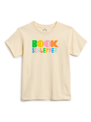 A light beige short-sleeve t-shirt with a colorful graphic on the chest that reads 'BOOK SCHLEPPER' in multicolored letters, displayed against a plain white background.