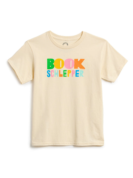A light beige short-sleeve t-shirt with a colorful graphic on the chest that reads 'BOOK SCHLEPPER' in multicolored letters, displayed against a plain white background.