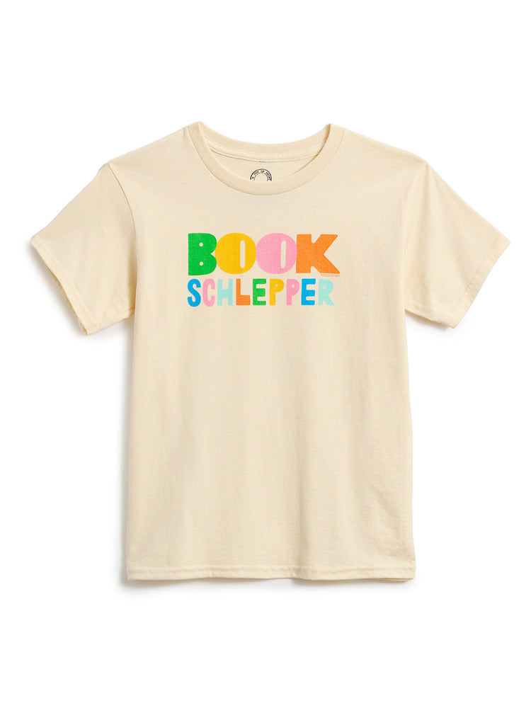 A light beige short-sleeve t-shirt with a colorful graphic on the chest that reads 'BOOK SCHLEPPER' in multicolored letters, displayed against a plain white background.