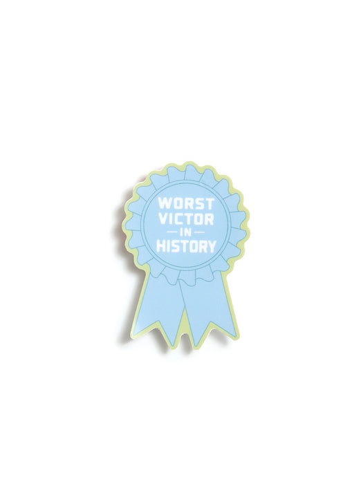 A light blue ribbon sticker with a pale yellow-green outline and white text reading 'WORST VICTOR IN HISTORY', shown on a plain white background.