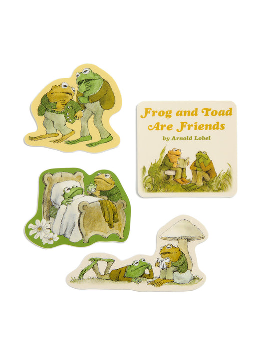 Four illustrated frog-themed items on a plain white background: two die-cut character stickers, a square book cover reading 'Frog and Toad Are Friends' by Arnold Lobel, and a small rounded patch or badge with a frog and mushroom scene.