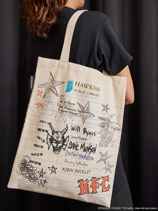Person holding a tote bag with 'Stranger Things' designs and text.