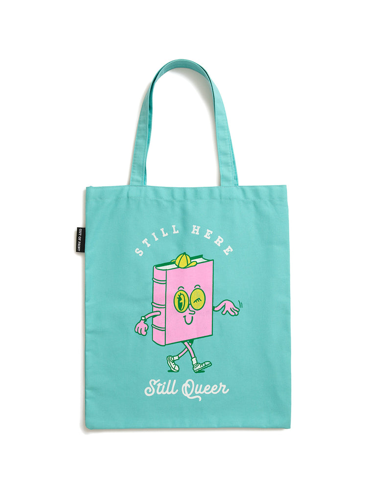 A light teal canvas tote bag featuring a cute pink book character with a smiling face, the words 'STILL HERE' above it, and 'Still Queer' written below in white script.