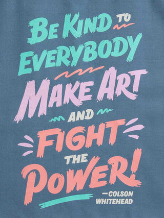A close-up of a blue fabric surface printed with colorful hand-lettered text reading 'Be Kind to Everybody, Make Art and Fight the Power! -Colson Whitehead'.